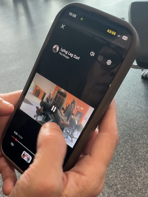A client watching Paul's lying leg curl demo in the app